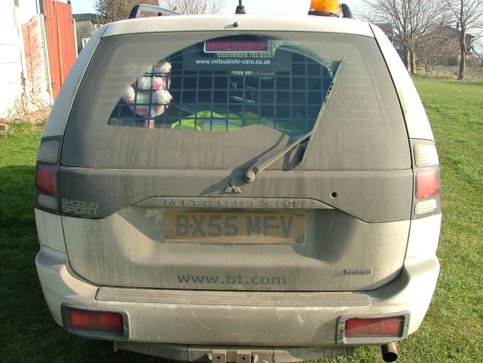Dirty silver Mitsubishi Shogun Sport SUV rear, UK plate BX55 MFV, caged window, parked on grass