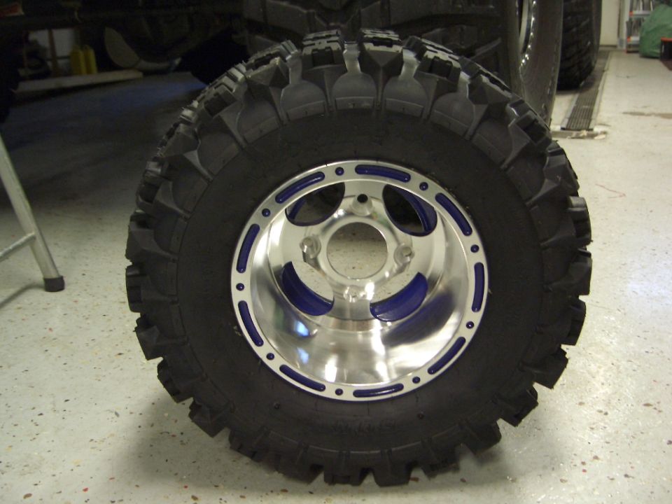 Close-up of a large off-road tire mounted on a polished aluminum wheel with blue accents