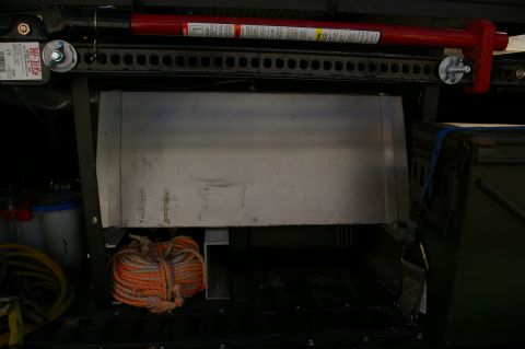 1986 Ford Bronco - A Hi-Lift jack is mounted above a storage compartment in a vehicle, with rope coiled below.