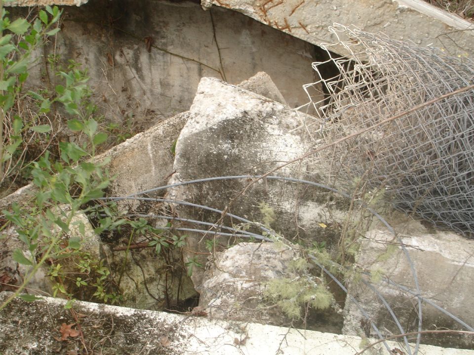 Pile of broken concrete chunks and twisted chain-link fence with overgrown weeds