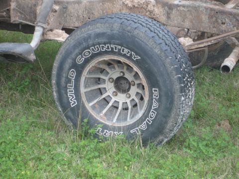 1989 Ford Bronco - A close-up view of a tire and part of the chassis of a vehicle, resting on grass.