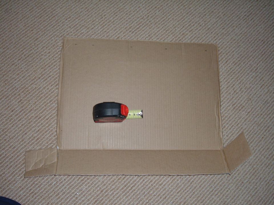 Cut cardboard template with folded flange and a tape measure on beige carpet