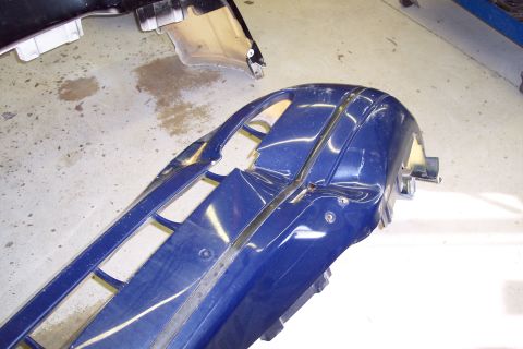 2001 Ford Crown Victoria - A blue car bumper and part of another car part are on a concrete floor.