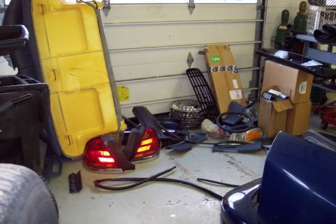 2001 Ford Crown Victoria - Various car parts are scattered around a garage floor, with a large garage door in the background.