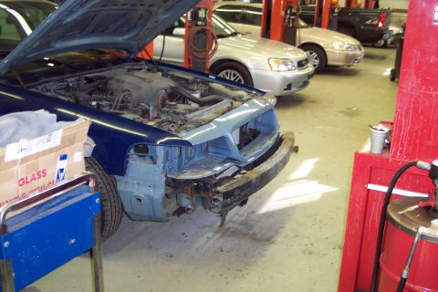 2001 Ford Crown Victoria - A blue sedan is in a garage with its hood up and front bumper removed, undergoing repairs.