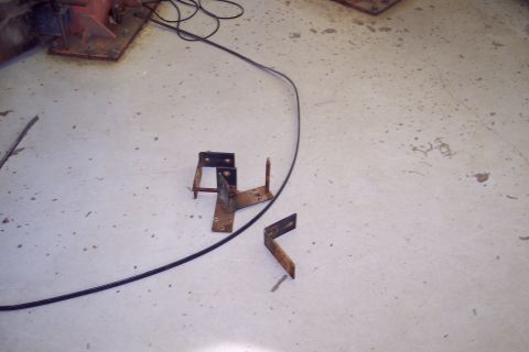 2001 Ford Crown Victoria - Several metal brackets and a black cable are scattered on a concrete floor.