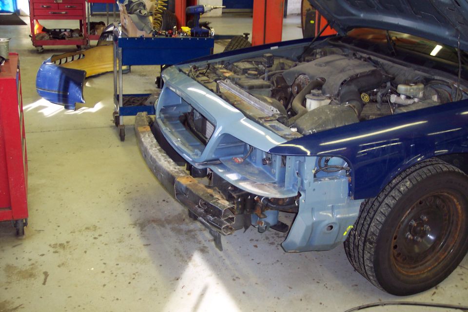 Blue 2001 Ford Crown Victoria front end damage, hood open, in repair shop