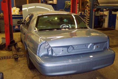 2001 Ford Crown Victoria - A blue sedan is parked in a garage with its hood open and rear bumper removed.