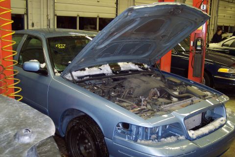 2001 Ford Crown Victoria - A blue sedan with its hood open and snow on its body sits in a garage, with another vehicle visible in the background.