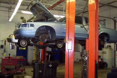 2001 Ford Crown Victoria - Light blue 2001 Ford Crown Victoria undergoing maintenance on a car lift in a service bay.
