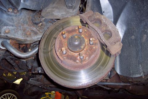 2001 Ford Crown Victoria - Underside view of a heavily rusted vehicle brake system, showing wear on the rotor and caliper.