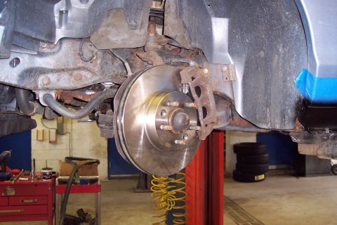 2001 Ford Crown Victoria - Front brake rotor and suspension components of a vehicle undergoing service in a garage.