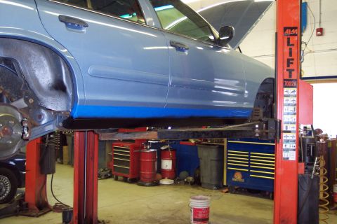 2001 Ford Crown Victoria - A blue sedan is raised on a car lift in a garage, with its hood open, revealing the engine bay.