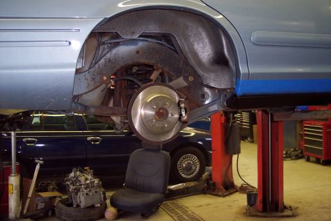 2001 Ford Crown Victoria - The rear suspension and wheel well of a light blue car are shown while it is elevated on a lift, with another vehicle beneath it.