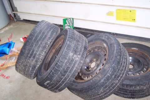 2001 Ford Crown Victoria - Four tires and rims are stacked on a garage floor, with a NAPA box visible.
