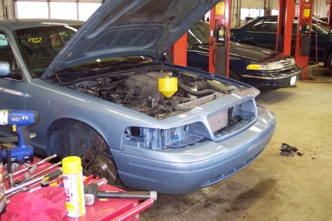 2001 Ford Crown Victoria - A blue sedan is in a garage with its hood open, surrounded by tools, with another vehicle parked behind it.