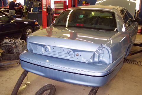 2001 Ford Crown Victoria - A light blue 2001 Ford Crown Victoria is seen from the rear in a garage, with its hood open and missing a taillight.