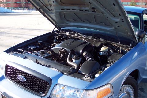 2001 Ford Crown Victoria - The engine bay of a blue Ford Crown Victoria is visible with the hood raised, revealing the V8 engine and front grille.