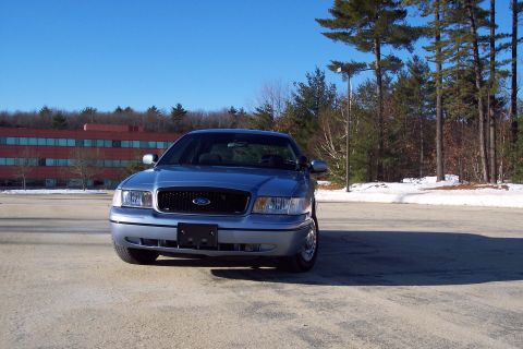 2001 Ford Crown Victoria - A blue Ford Crown Victoria is parked in a lot with snow on the ground and trees in the background.