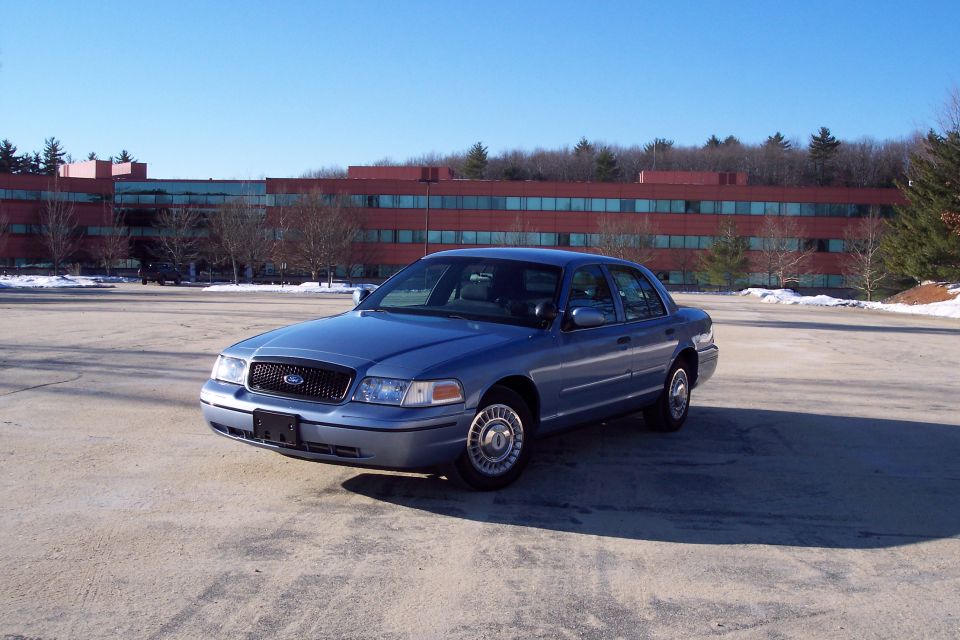 Blue 2001 Ford Crown Victoria parked in a lot with a red brick building in the background