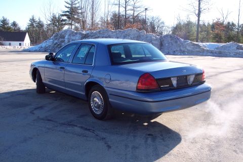 2001 Ford Crown Victoria - A blue 2001 Ford Crown Victoria sedan is viewed from the rear 3/4 angle, emitting exhaust smoke.