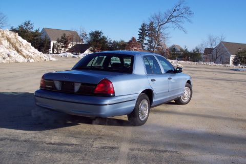 2001 Ford Crown Victoria - A light blue sedan is parked in a lot on a clear day with snow visible.