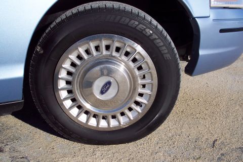 2001 Ford Crown Victoria - Front wheel and fender of a 2001 Ford Crown Victoria, showing the hubcap and tire tread.