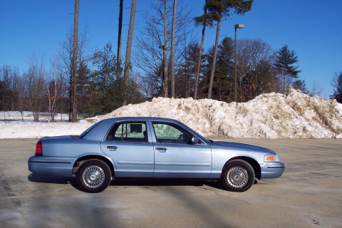 2001 Ford Crown Victoria - A light blue 2001 Ford Crown Victoria is parked on a paved surface with a large snow pile behind it.