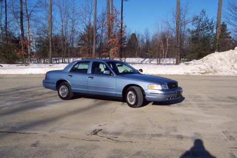 2001 Ford Crown Victoria - A blue 2001 Ford Crown Victoria sedan is parked outdoors in a lot with trees and snow visible.