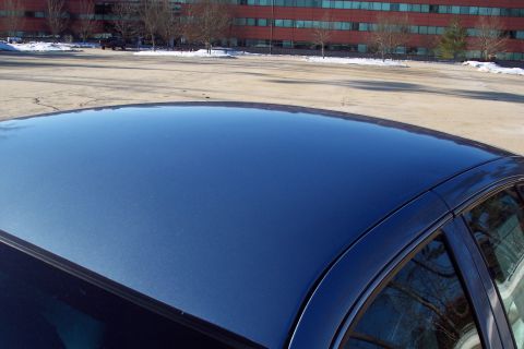 2001 Ford Crown Victoria - A blue sedan's roof is shown in the foreground, with a building and trees in the background.