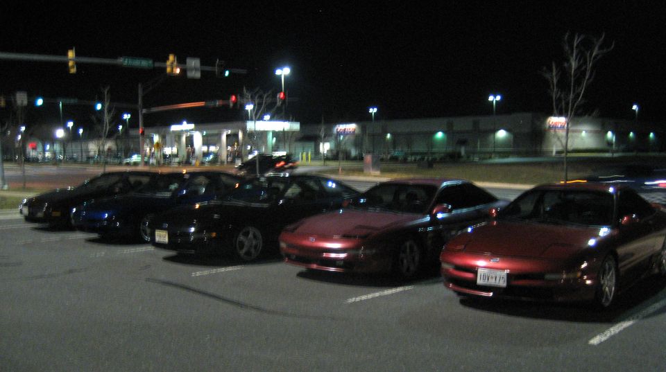 Several red and black Ford Probes parked at night in a parking lot