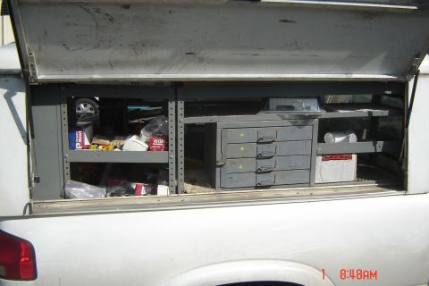 2006 Honda CBR-RR - The open bed of a white truck reveals organized storage compartments filled with various items and tools.