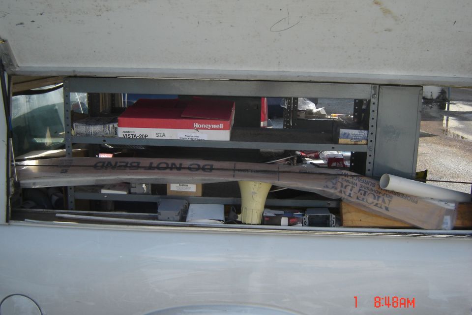 Shelving unit in a truck bed filled with boxes, pipes, and other items. Text on a pipe reads 'DO NOT BEND'