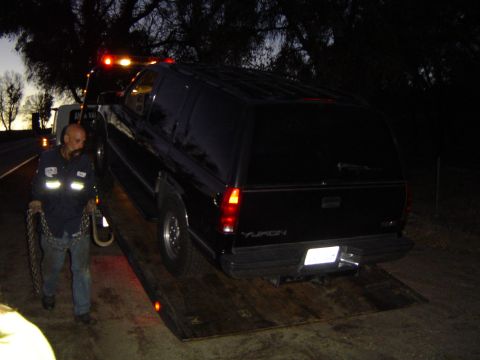 1989 Ford Bronco - A black SUV, identified as a Yukon, is loaded onto a tow truck as dusk settles.