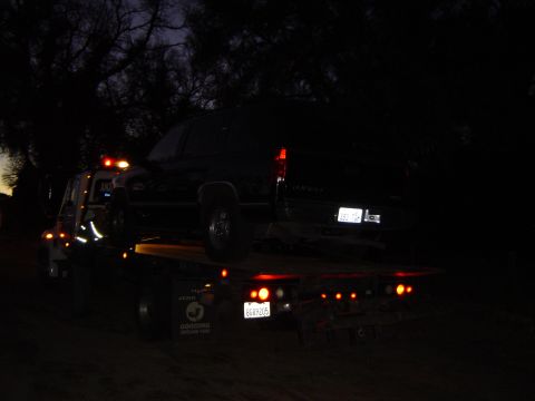 1989 Ford Bronco - Tow truck transporting a black SUV at night, with its hazard lights illuminated.