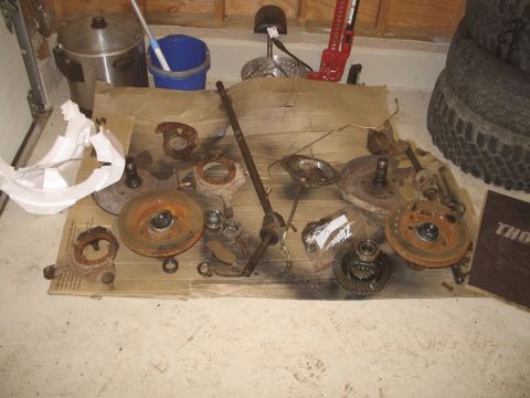 1995 Ford Bronco - Various vehicle components, such as axles, brake rotors, and a differential, are spread out on a piece of cardboard.