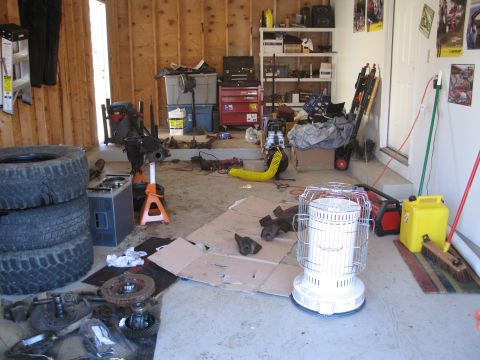 1995 Ford Bronco - A cluttered garage scene with various vehicle parts and tools scattered around, including stacked tires and a heater.