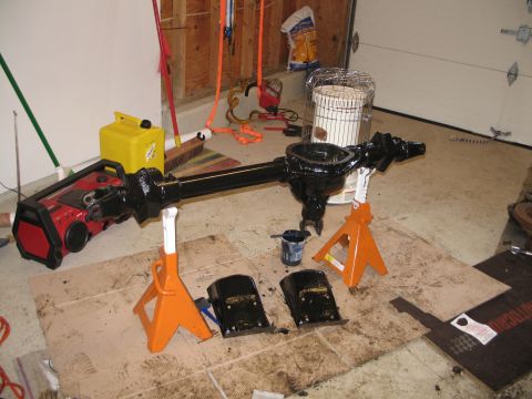 1995 Ford Bronco - A black axle assembly is supported by jack stands, with parts and painting supplies laid out on the floor.