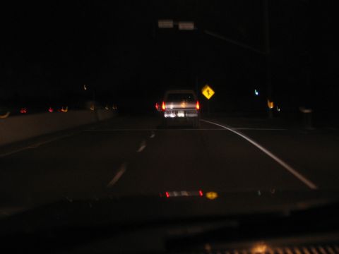 1989 Ford Bronco - A vehicle travels down a dark highway at night, with a yellow diamond warning sign visible on the right side of the road.