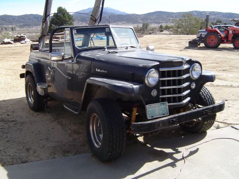 1989 Ford Bronco - This black Jeep CJ-5, likely from the mid-1950s, sits in a dusty outdoor lot.