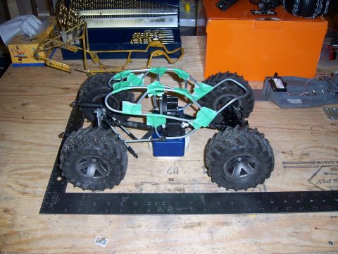 1996 Ford Bronco - RC car chassis with large tires and a green taped roll cage sits on a workbench.