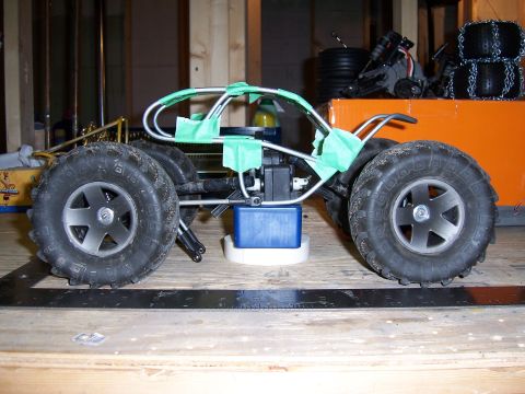 1996 Ford Bronco - Side view of a remote control car chassis, large off-road tires and a metal frame secured with green tape.