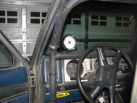 1984 Ford Bronco II - An aftermarket gauge is mounted on the roll cage inside the vehicle, with a garage door visible through the windshield.