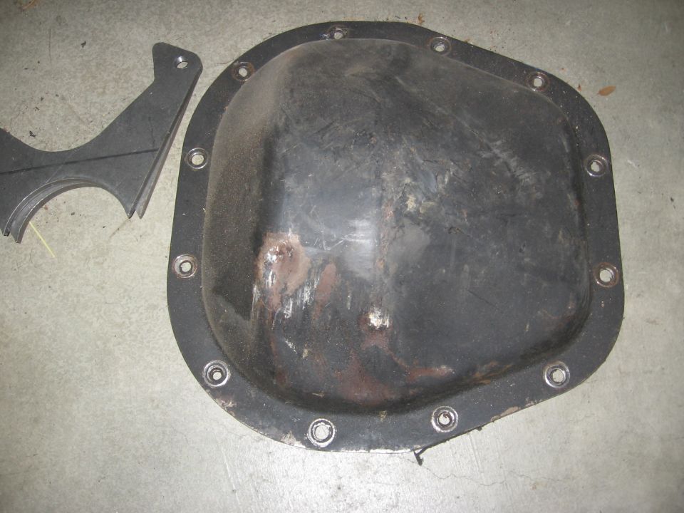 Black differential cover with rust spots and a metal bracket on a concrete floor