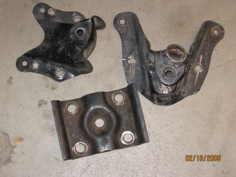 1994 Ford Bronco - Three metal brackets are shown on a concrete floor, likely automotive parts.