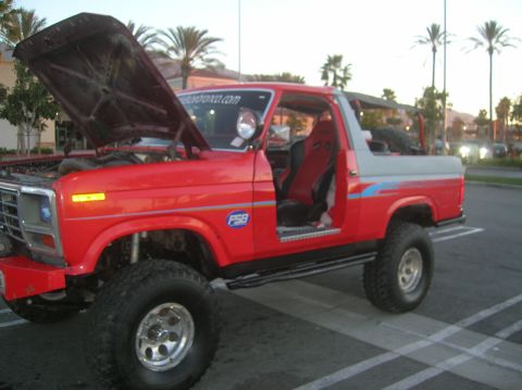 1985 Ford Bronco - This 1985 Ford Bronco features a lifted suspension, off-road tires, and racing seats visible through the open driver's door.