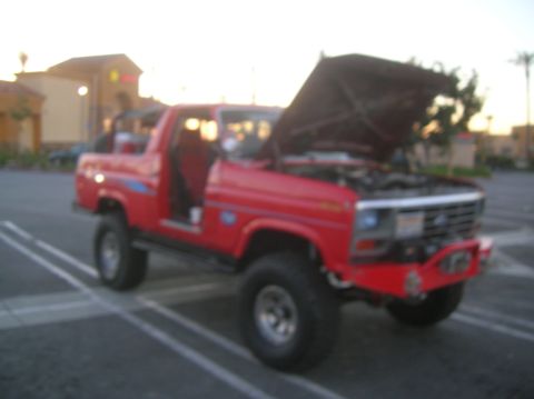 1985 Ford Bronco - Red pickup truck with hood open, parked in a lot at sunset.