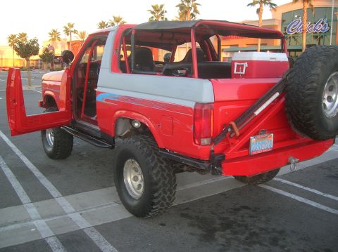 1985 Ford Bronco - This red SUV features off-road tires, a lifted suspension, and a spare tire mounted on the rear.