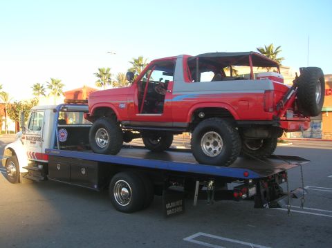 1985 Ford Bronco - A red and grey 1985 Ford Bronco, with its doors removed, is loaded onto a tow truck.