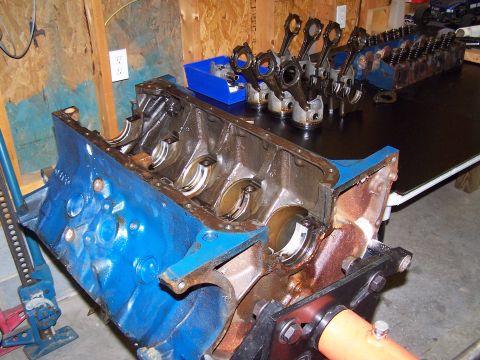 1974 Ford F-100 - Disassembled engine components, including a blue engine block and pistons with connecting rods, are arranged on a workbench.